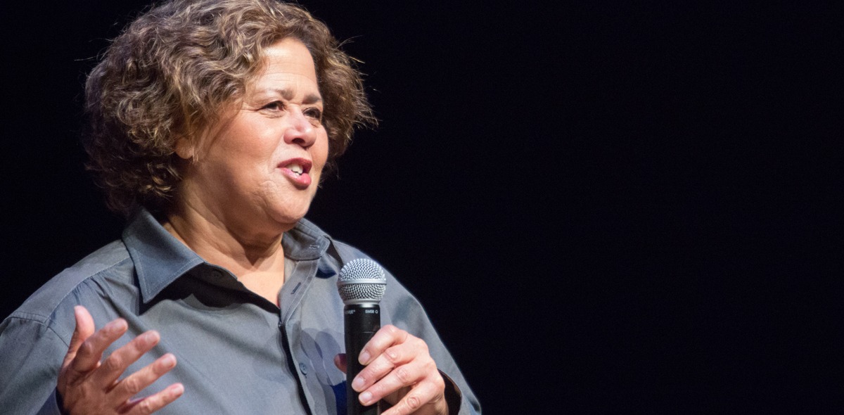 Anna Deavere Smith holds a microphone and gestures with her right hand as she speaks