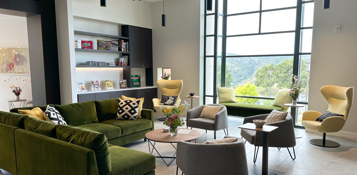 Interior shot of new Global Language and Culture Center featuring gray and green chairs, a velvet green couch, a bookcase with magazines, and a kitchen