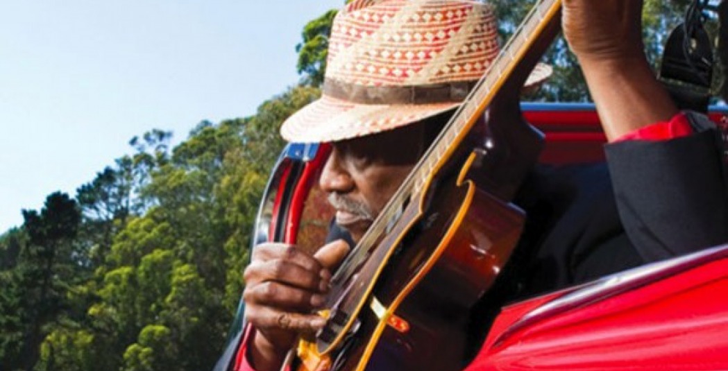 Taj Mahal sitting in red car with guitar