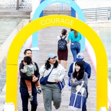 A group of people walk under colorful arches that display "Wisdom, Compassion, and Courage" during the Soka Peace Festival