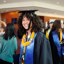 A graduate wearing her cap and gown smiles at the camera after commencement