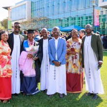 A family dressed in traditional formal attire smiles with their graduate after the commencement ceremony