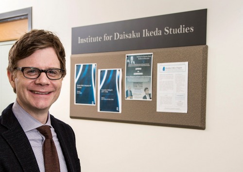 Jason Goulah stands in front of Institute for Daisaku Ikeda Studies bulletin board