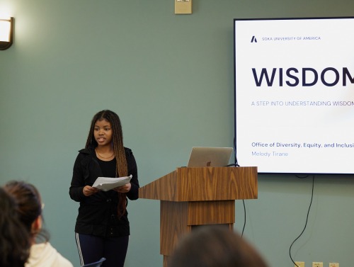 A speaker stands beside the podium as she presents during a seminar series