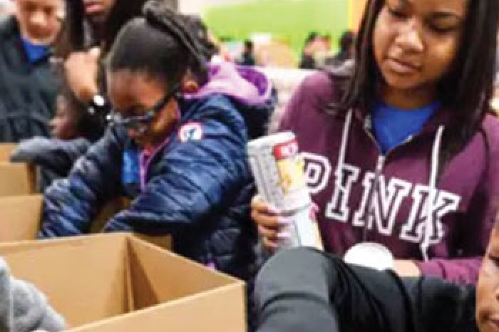 Children pack boxes of food while volunteering.