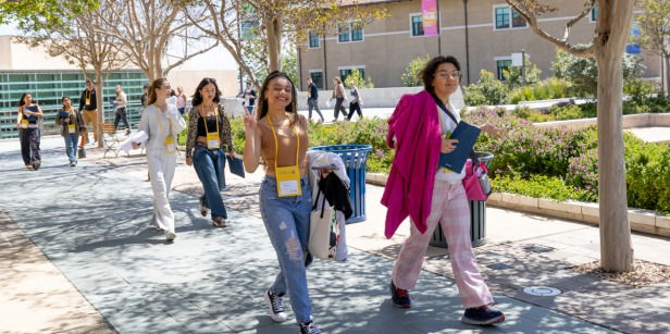A group of young students walks along a paved, tree-lined path on sunny Soka University campus.
