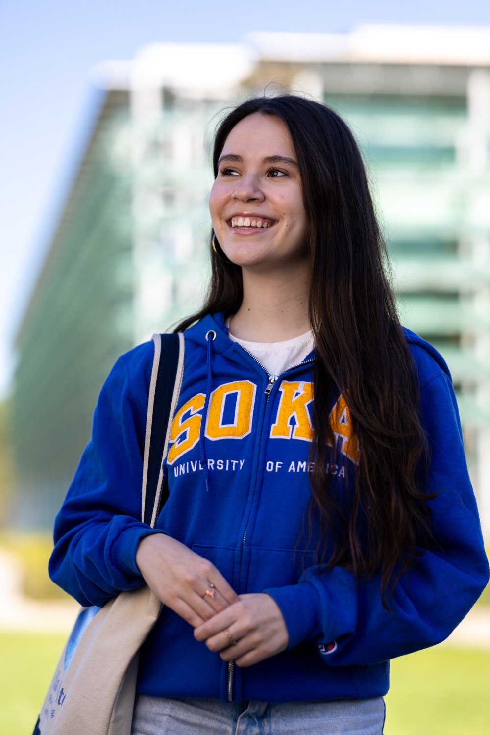 Valentina Ferreira Einsfeld '26 wears a blue hoodie that says "Soka" in yellow lettering and she smiles off into the distance on SUA's campus.