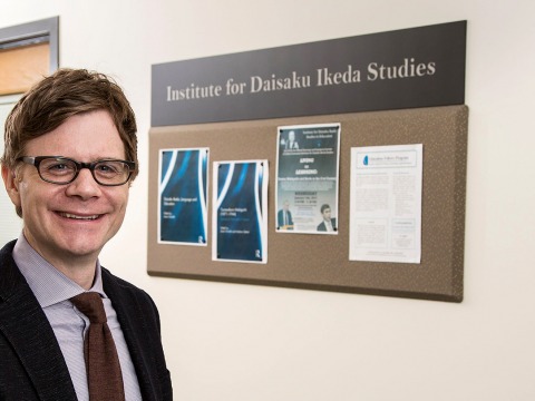 Jason Goulah stands in front of Institute for Daisaku Ikeda Studies bulletin board