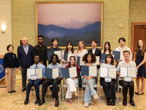 A large group of students hold up their academic awards and pose alongside university faculty and leadership.