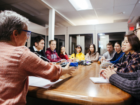 A group of 11 people sit around an oval wooden table and take part in a discussion.