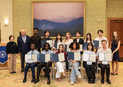 A large group of students hold up their academic awards and pose alongside university faculty and leadership.