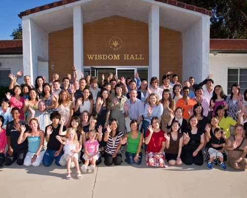 A group of people wave to the camera outside of Wisdom Hall